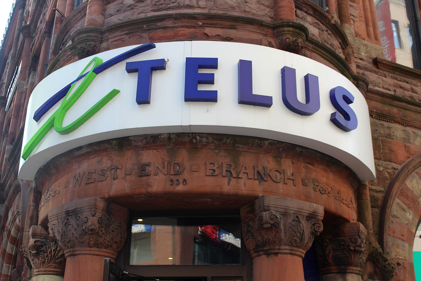 Laminated raparound Telus signage covers the original art-nouveau lettering above the door of what was formerly the Bank of Montreal.